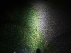 Photo showing gravel in the dark, lit up by a bike light, with the front wheel of the bike just visible