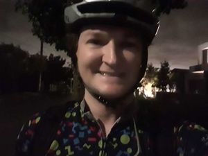 A picture of me in the dark, grinning, wearing a bike helmet and bike jersey